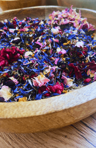 Un mélange de thé personnalisé avec des fleurs et des fruits séchés, présenté dans un bol en bois.