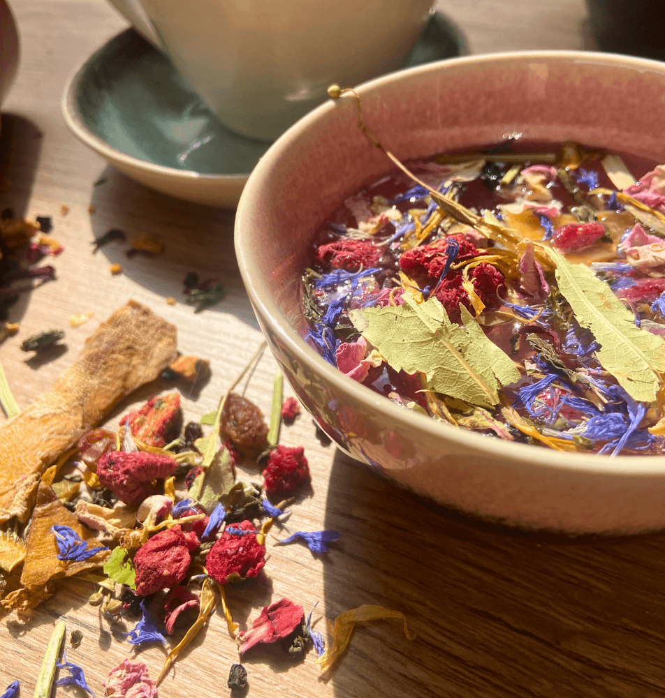 Tasse de thé personnalisé avec des ingrédients naturels comme des fleurs, des feuilles et des fruits secs, sur une table en bois - My Own Tea